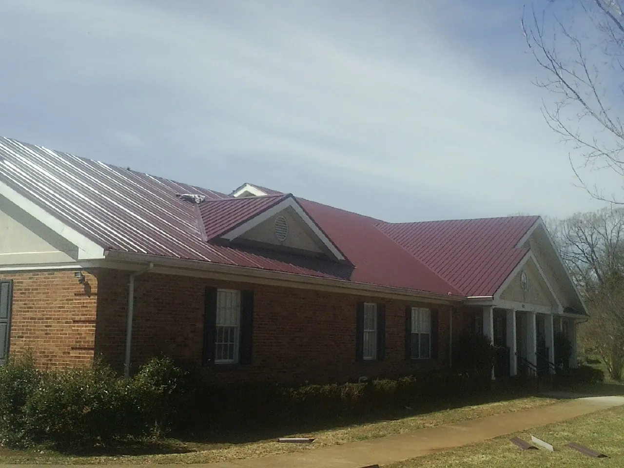Red metal roof with gabled entries on a long brick building, from a Hail Damage Roof Repair job in Morristown