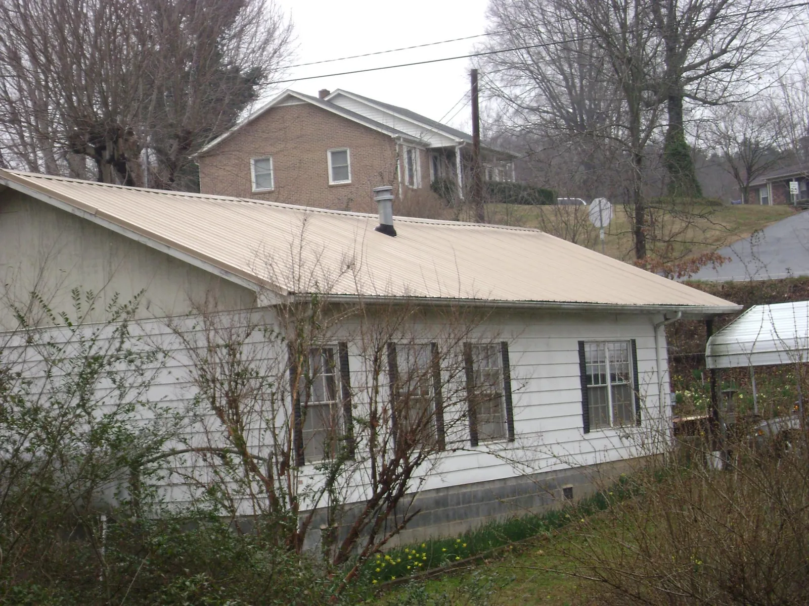 Tan metal roof on a white sided house set into a hillside — Commercial Roofing by Roofing Brothers in Morristown
